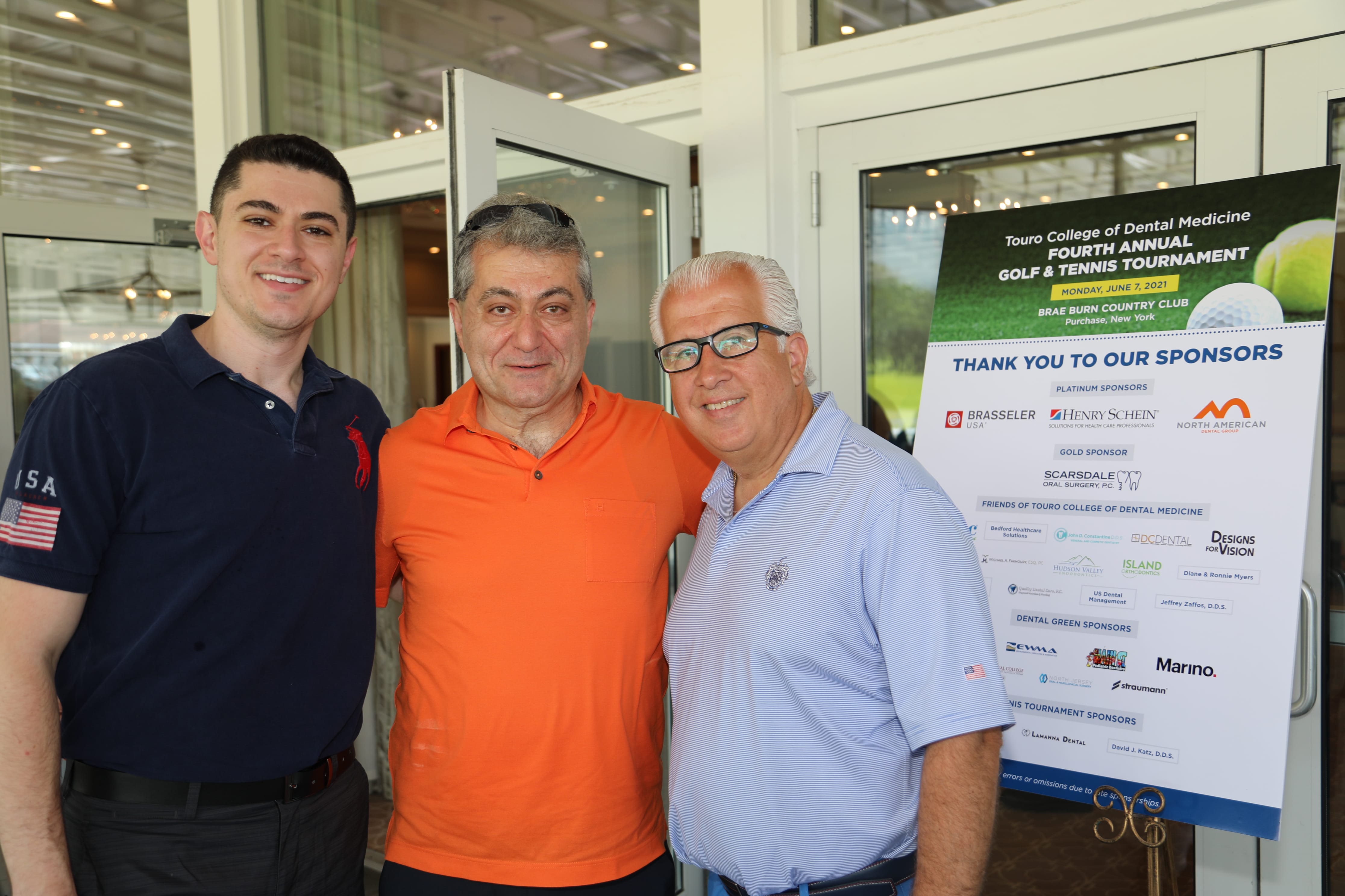 golf attendees posing in front of sponsorship board