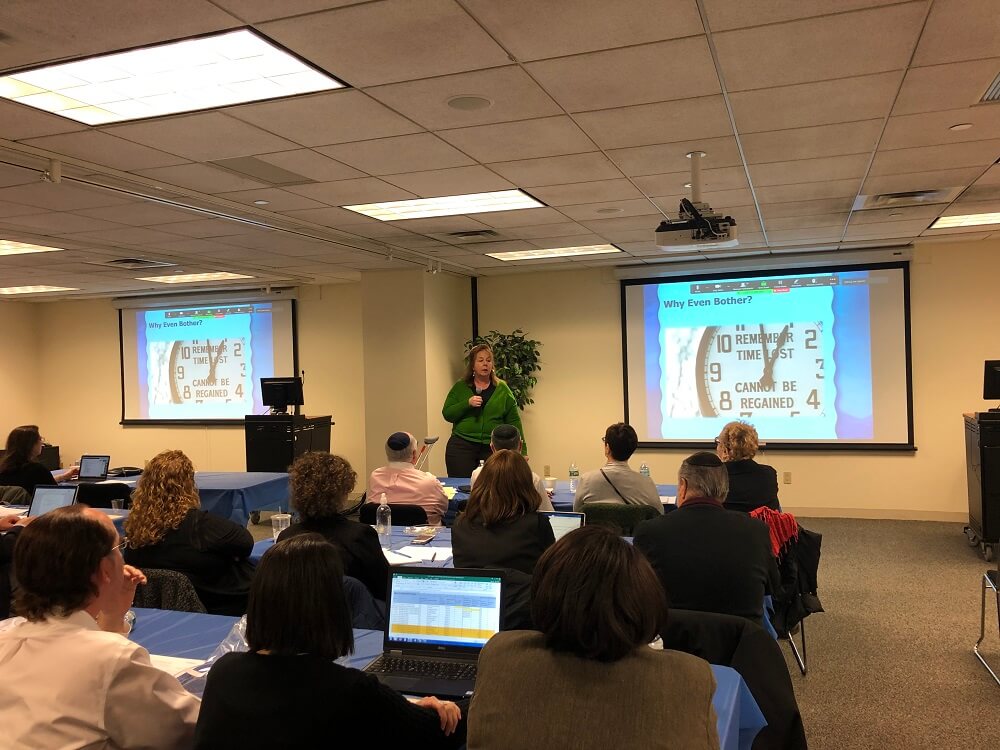 View from the back of the room of attendings and two screens during a presentation at the Assessment Summit.