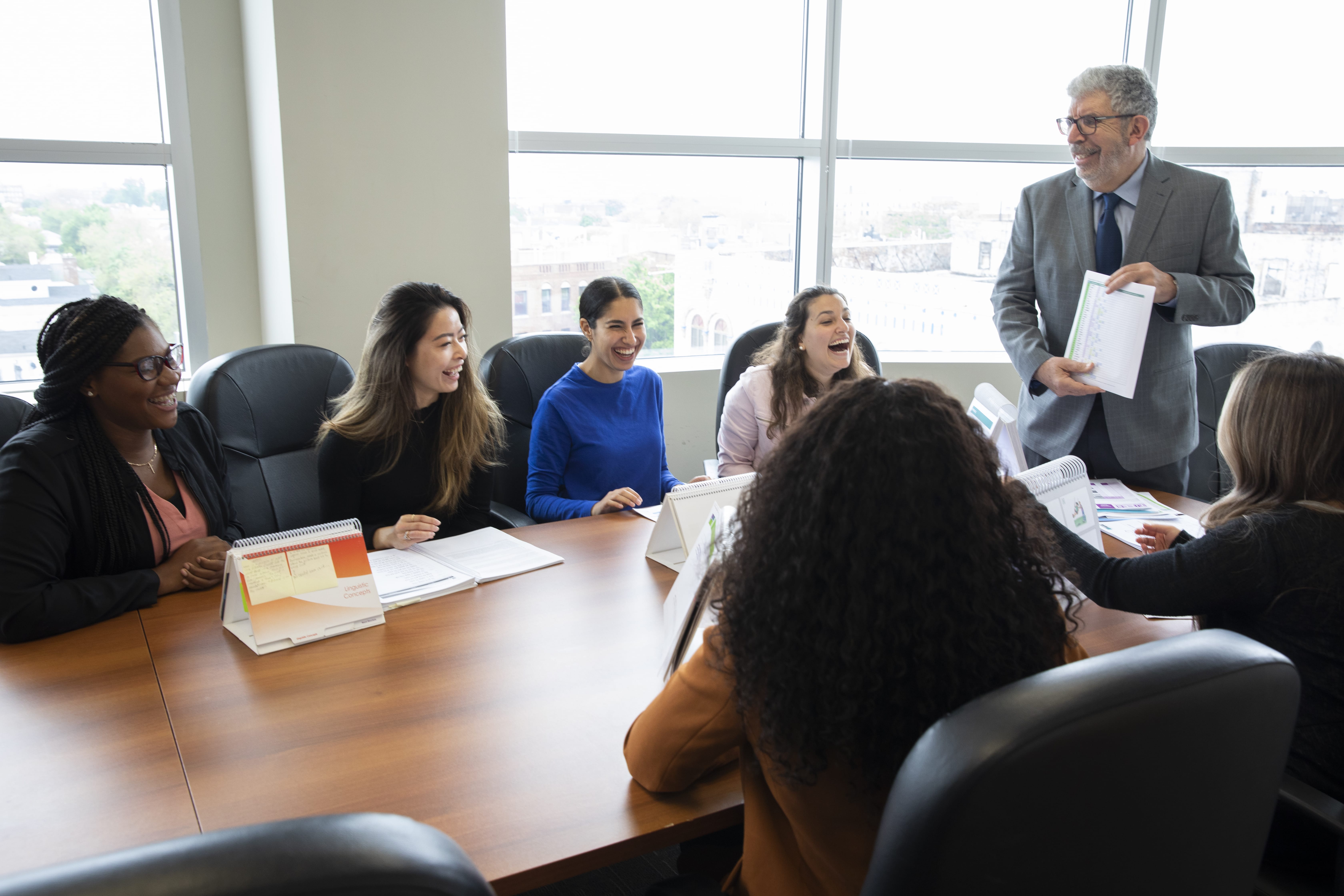 SLP students sitting around a conference table with a teacher teaching the class