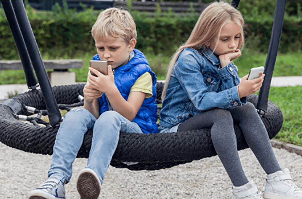 children sitting on a swing looking at their smartphones