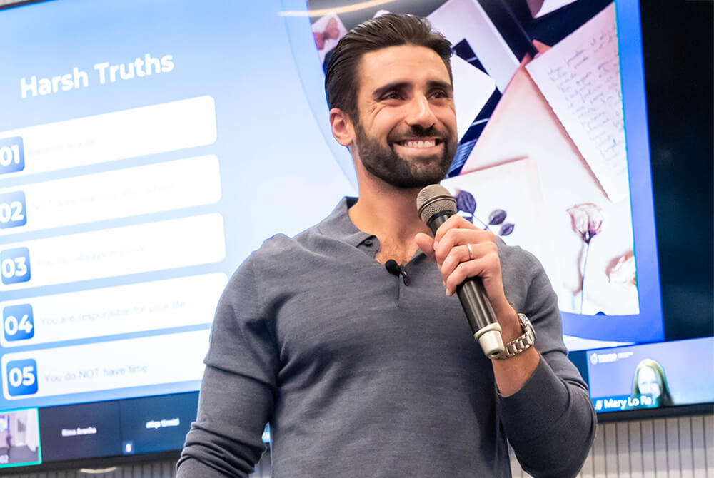 Jonathan Z Cohen, smiling and speaking in front of a presentation on a screen, holding a microphone