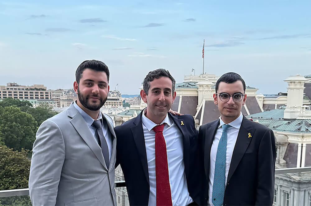 3 men in suits, Professor Mark Goldfeder, center, with a student on each side, wearing yellow pins standing in washington dc