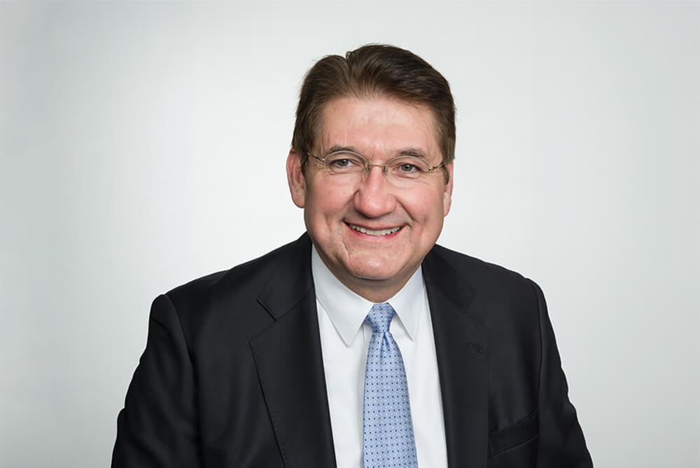 Larry Singleton, headshot of a man in a black suit, white shirt and blue tie