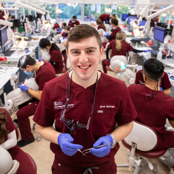 Jacob Buchinger smiling and holding dental tools in front of peers in dental practice lab