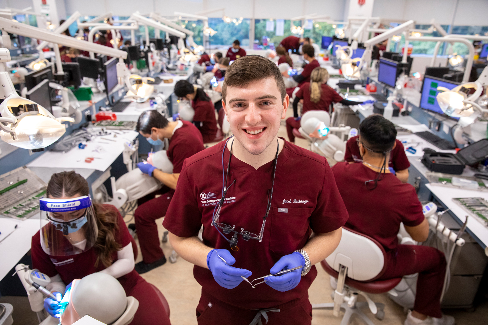 Jacob Buchinger smiling and holding dental tools in front of peers in dental practice lab