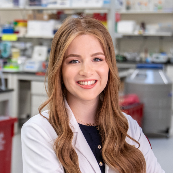 Julia Maron, wearing white coat, smiles and poses in NYMC medical lab