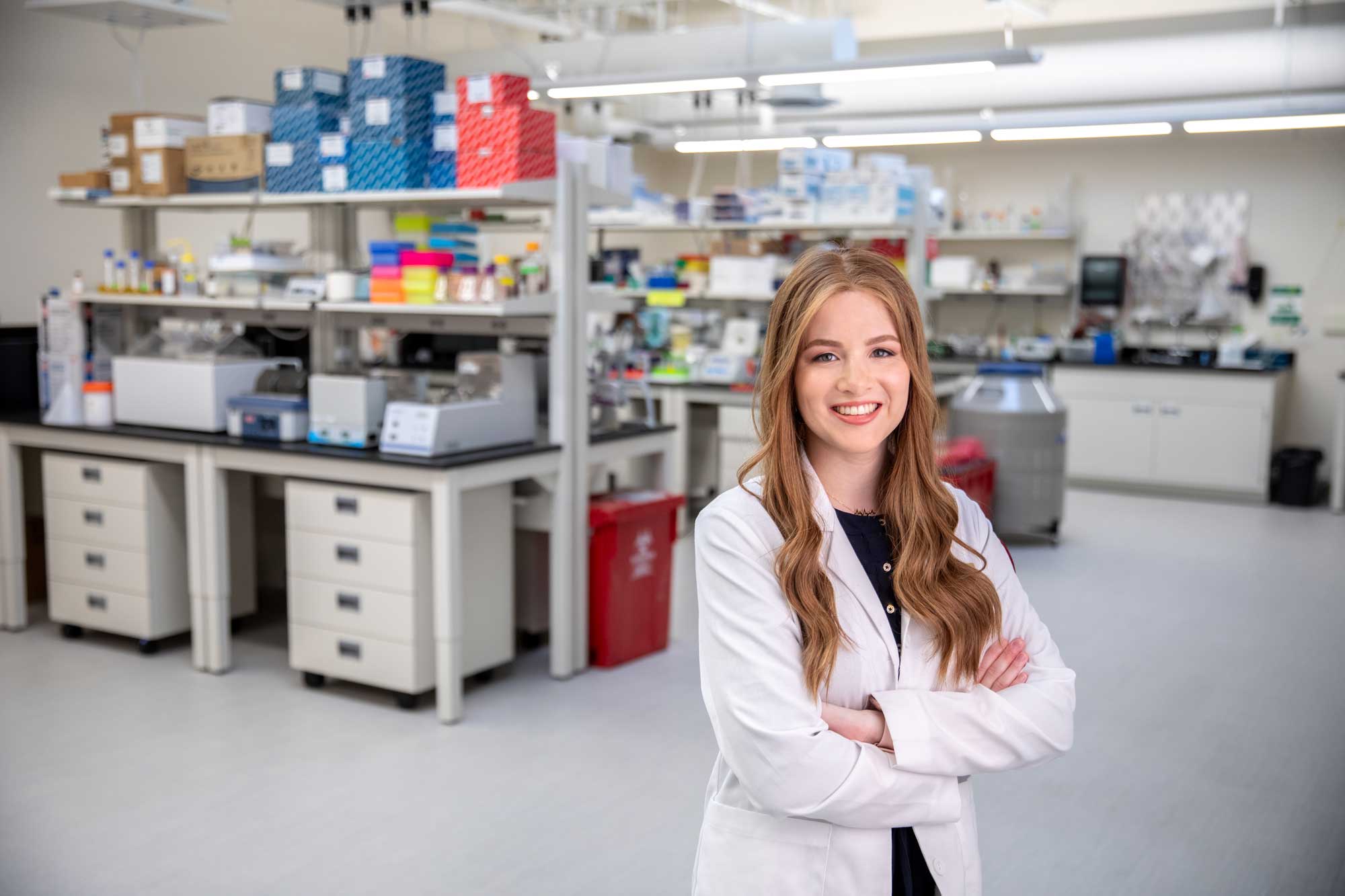 Julia Maron, wearing white coat, smiles and poses in NYMC medical lab