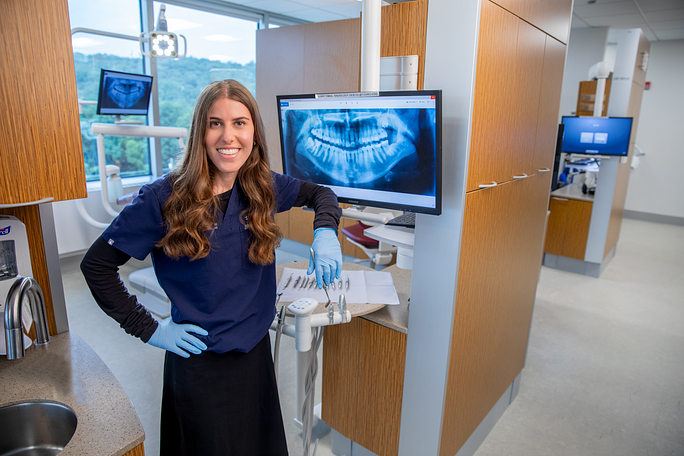 Lauren Salomon smiles next to dental equipment in TCDM clinic