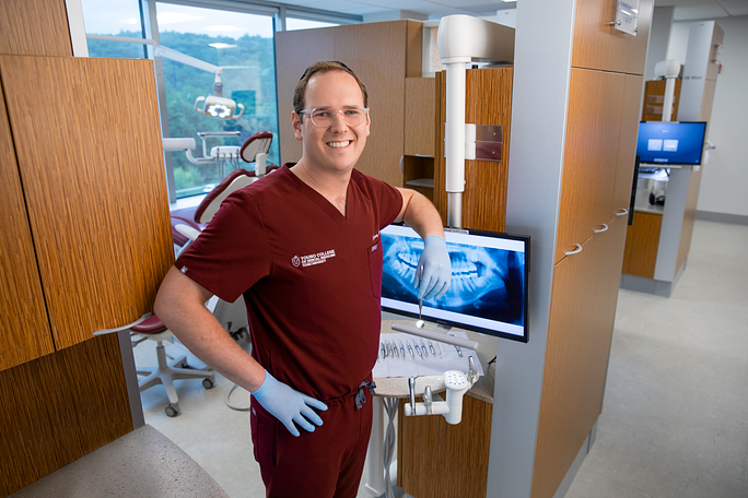 Zachary Mann smiles next to dental equipment in TCDM clinic