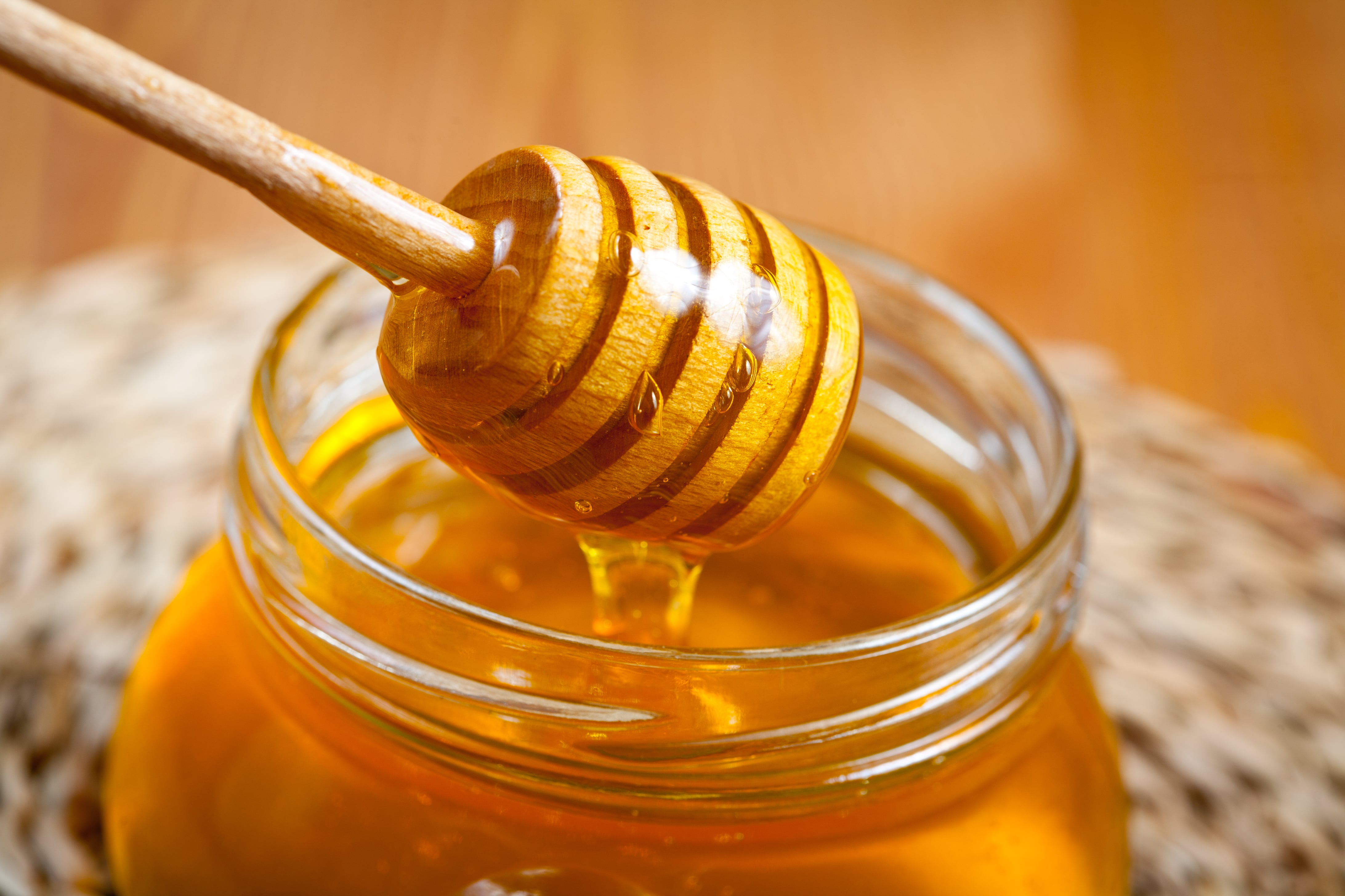 Wooden honey dipper dripping honey over a jar of honey.